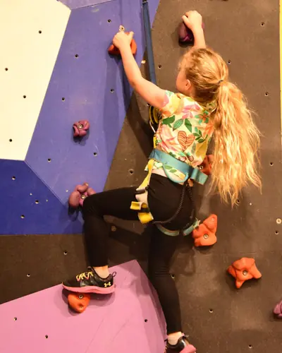 A girl with a long ponytail climbing a purple and blue wall