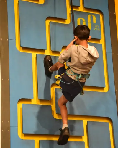 A boy climbing the blue and yellow maze wall