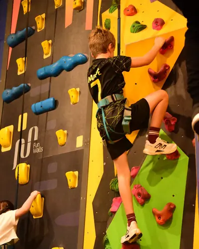 A boy reaching for the next hold on a yellow and green Fun Wall