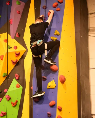An older boy halfway up a blue and yellow wall